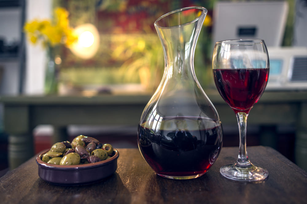 carafe of red wine with glass of red wine and bowl of olives