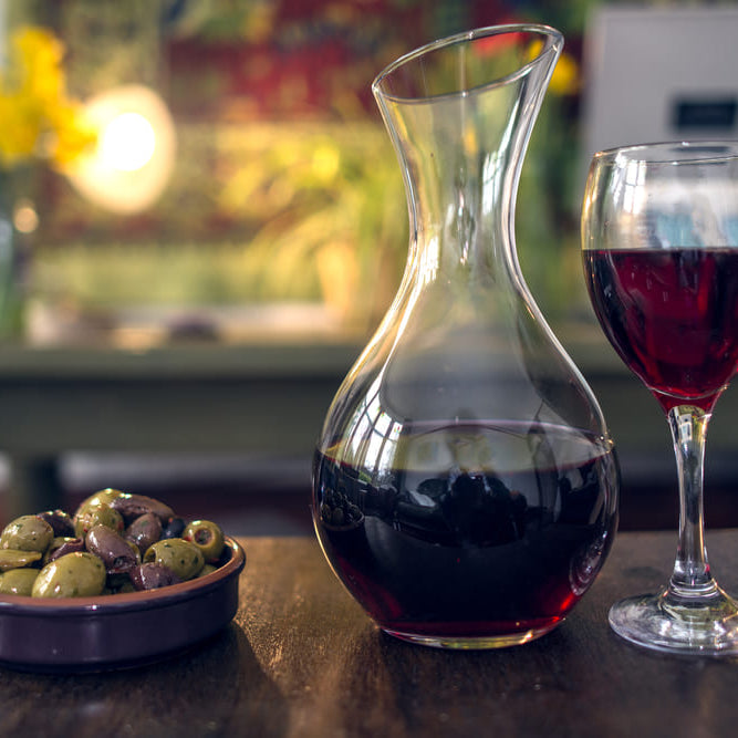 carafe of red wine with glass of red wine and bowl of olives